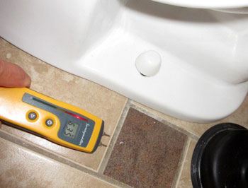 Moisture meter indicates elevated readings to floor by toilet